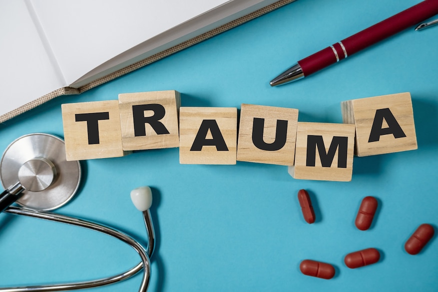 Stack of wooden blocks spell out the word trauma. There are also a few pills and a pen on the table