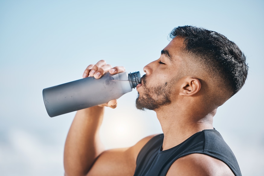 Fitness, man and drinking water outdoors after training, running or morning cardio routine. Thirst, hydration and Indian male runner with bottle drink after sports, workout and body performance