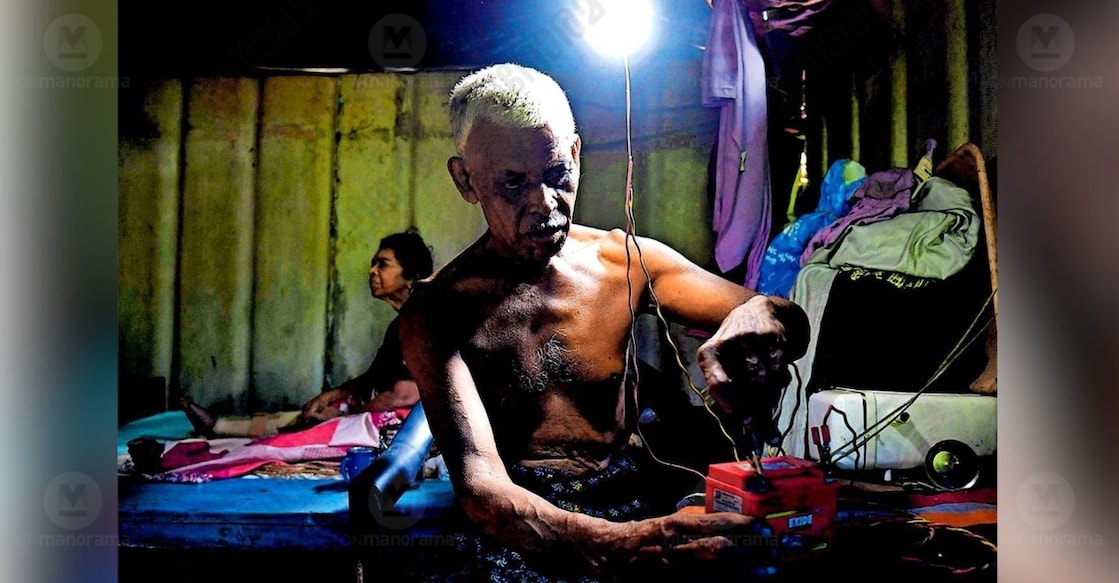 Malayil Raveendran and his wife, Ramani, live in a fragile single-room home walled with asbestos sheets—a structure on the verge of collapse at any moment. Ramani is visually impaired. Inside, their sole source of light is a lone bulb wired to an old scooter battery, gifted by a generous neighbour. Photo: Vishnu Sanal / Manorama
