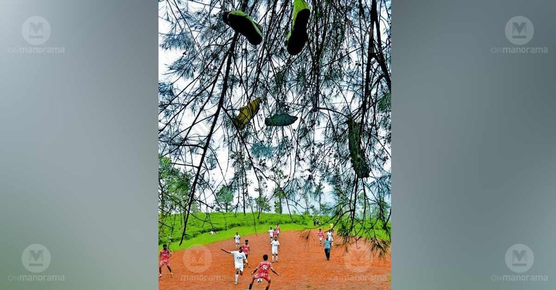 The Boot Tree… At the estate ground in Perumthatta, Kalpetta, memories of football sway in the wind from the branches of a windmill tree. Broken and worn-out boots of players who have played here for years now hang from its branches, giving the place its popular name, the ‘Boot Tree.’ A view of players in action with the Boot Tree in the foreground. Photo: Special arrangement