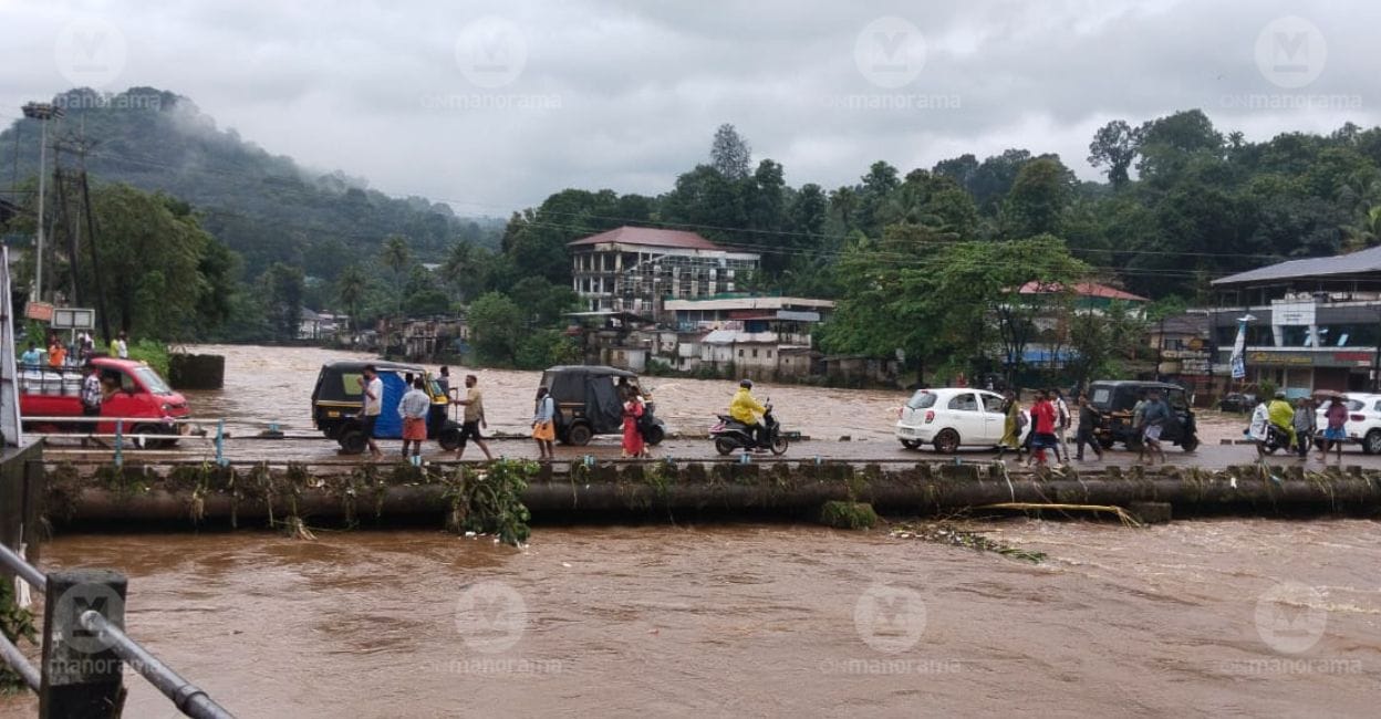Vehicles and pedestrians cross the Mundakkayam causeway as the river continues to swell following heavy rain on Saturday. Photo: Manorama. 