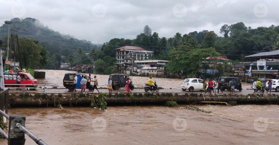 Vehicles and pedestrians cross the Mundakkayam causeway as the river continues to swell following heavy rain on Saturday. Photo: Manorama. 
