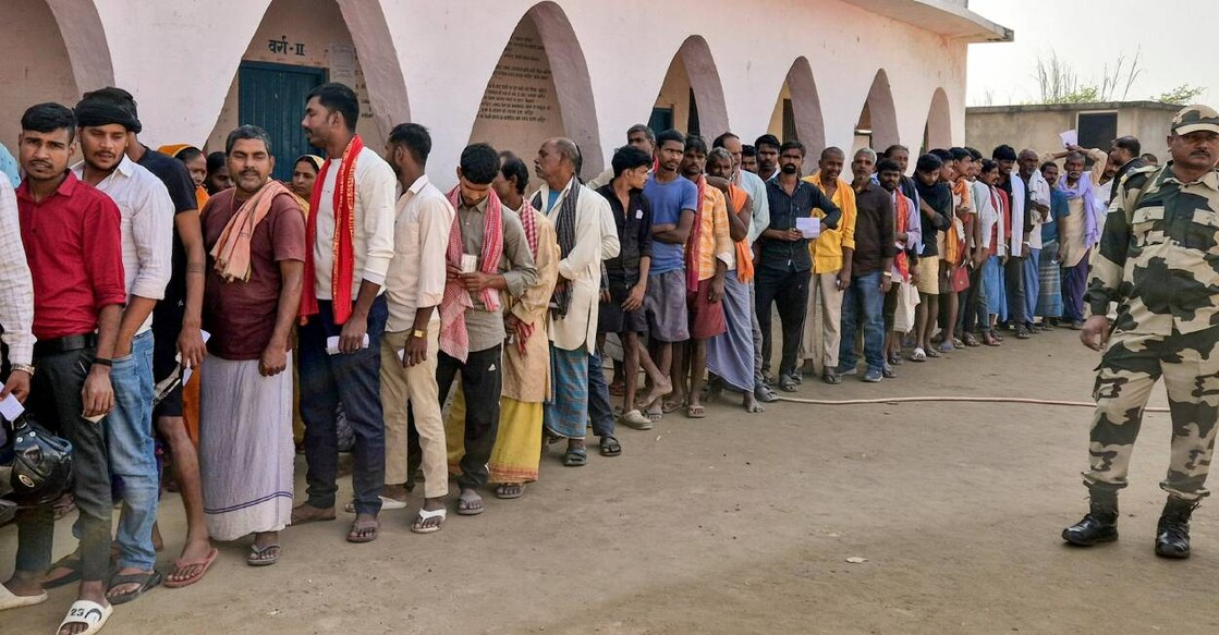 Security personnel keeps vigil as voters wait in a queue to cast votes at a polling station during the first phase of the Bihar Assembly elections. Photo: PTI