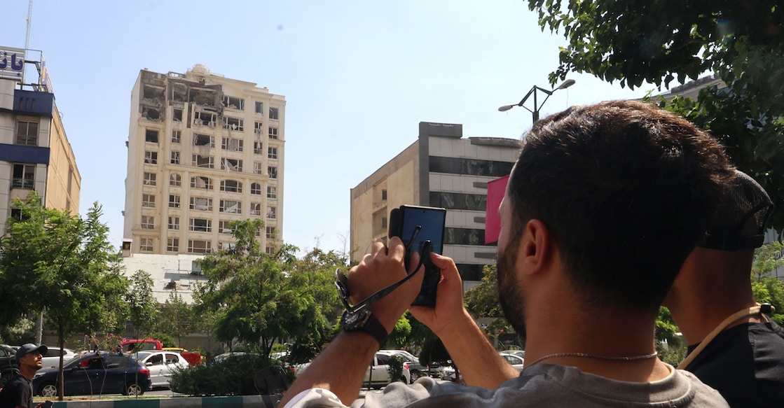 israel-iran-conflict A man takes a picture of a building damaged in an Israeli strike on Tehran on June 13, 2025. Photo: AFP/Atta KENARE