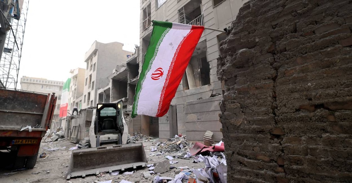 An Iranian flag flutters as as digger arrives to help remove the debris from destroyed buildings following a military strike on the Iranian capital Tehran on March 15, 2026. Photo: AFP