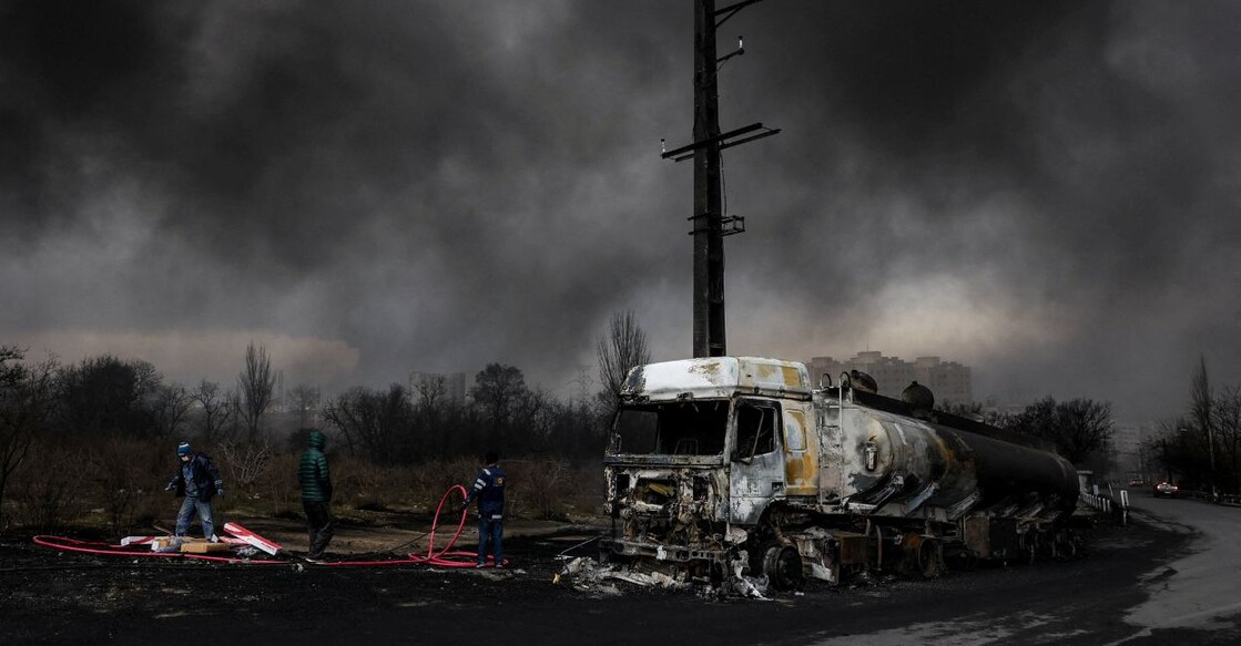 People stand near a destroyed vehicle as smoke rises after a reported strike on Shahran fuel tanks, amid the US-Israeli conflict with Iran. Photo: Majid Asgaripour/WANA (West Asia News Agency) via REUTERS