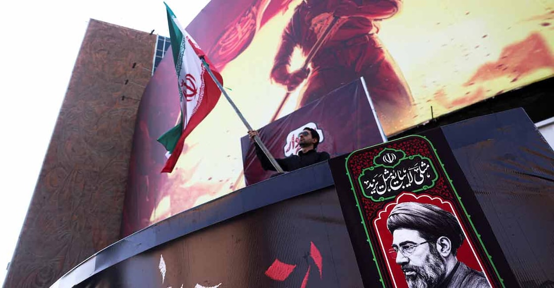 A man holds an Iranian flag, next to a picture of Iran's Supreme Leader Mojtaba Khamenei, in Tehran, Iran, August 13, 2026. Photo: Majid Asgaripour/WANA via REUTERS