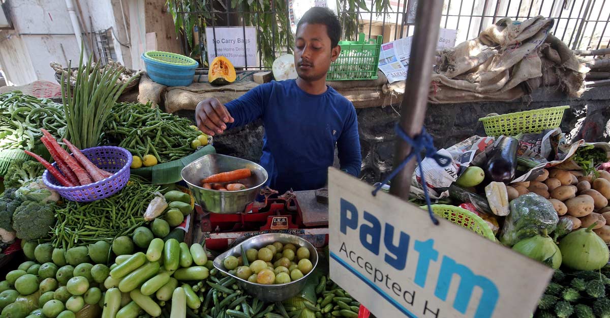 A vendor weighs vegetable next to an advertisement of Paytm, a digital payments firm, hanging amidst his vegetables at a roadside market in Mumbai, India, April 2, 2019. REUTERS/Francis Mascarenhas/File Photo