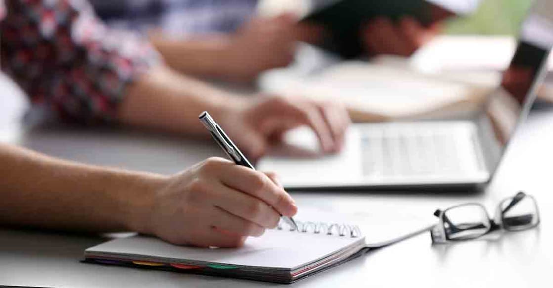 Student's hand writing in exercise book at the table