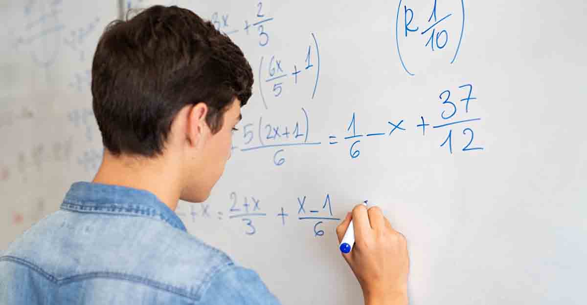 Back view of high school student solving math problem on whiteboard in classroom. Young man writing math solution on white board using marker. College guy solving math expression during lesson.