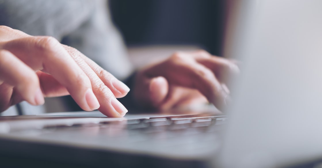 Closeup image of a business woman's hands working and typing on laptop keyboard on glass table