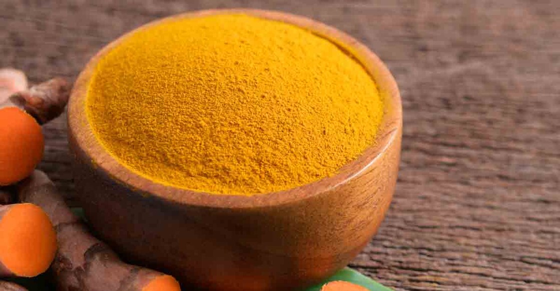 Turmeric powder in a wooden bowl and fresh turmeric (curcumin) on wooden background,copy space.