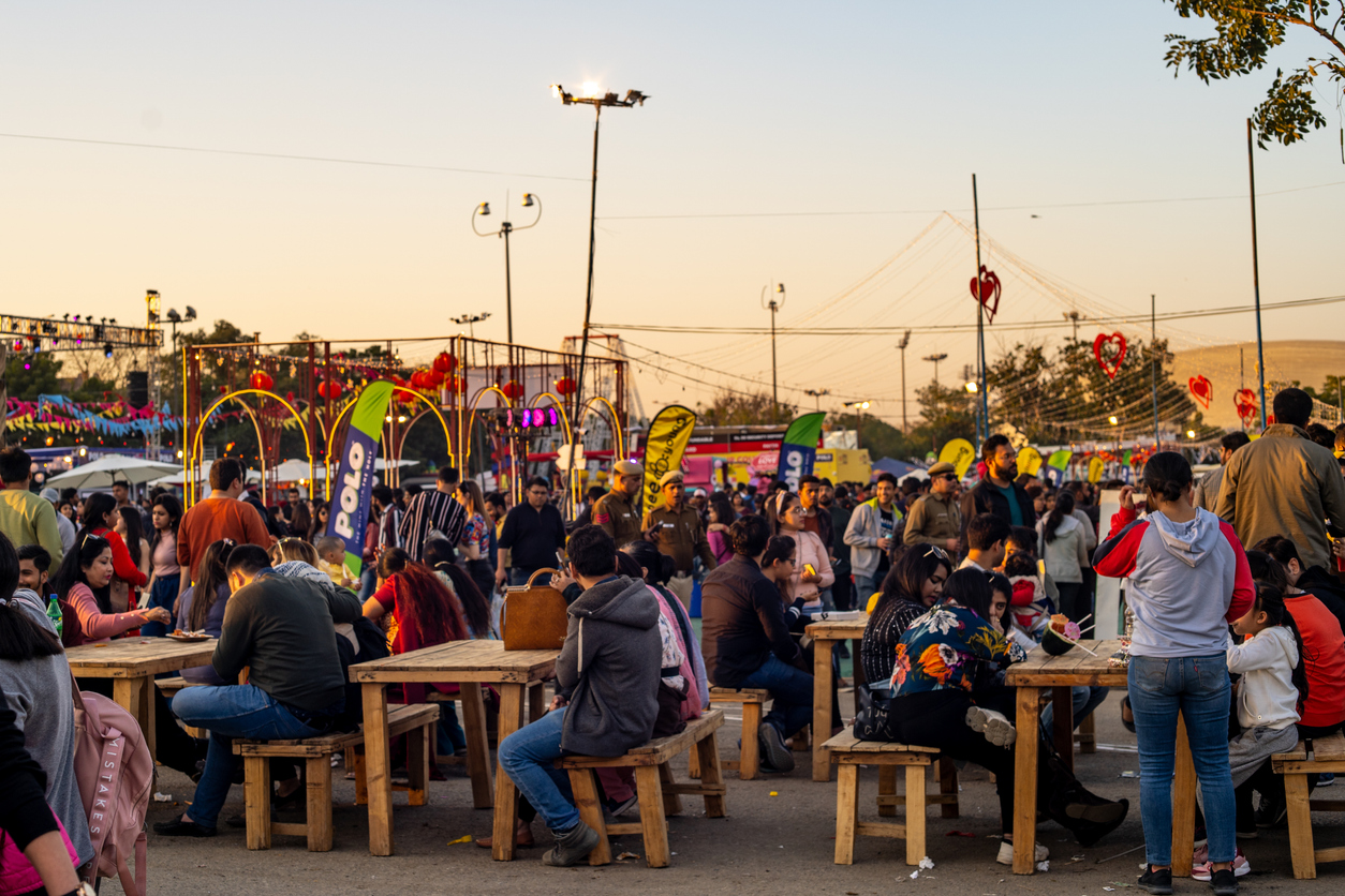 1207959930 Delhi, India - circa 2020 : Panning shot of crowd of people roaming around sitting on old tables and benches while they eat at the horn ok food truck festival. The various stall around and the huge crowd of men women children can be seen