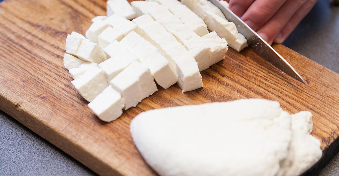 Cutting paneer into pieces on wooden board. Photo: iStock/liubomirt