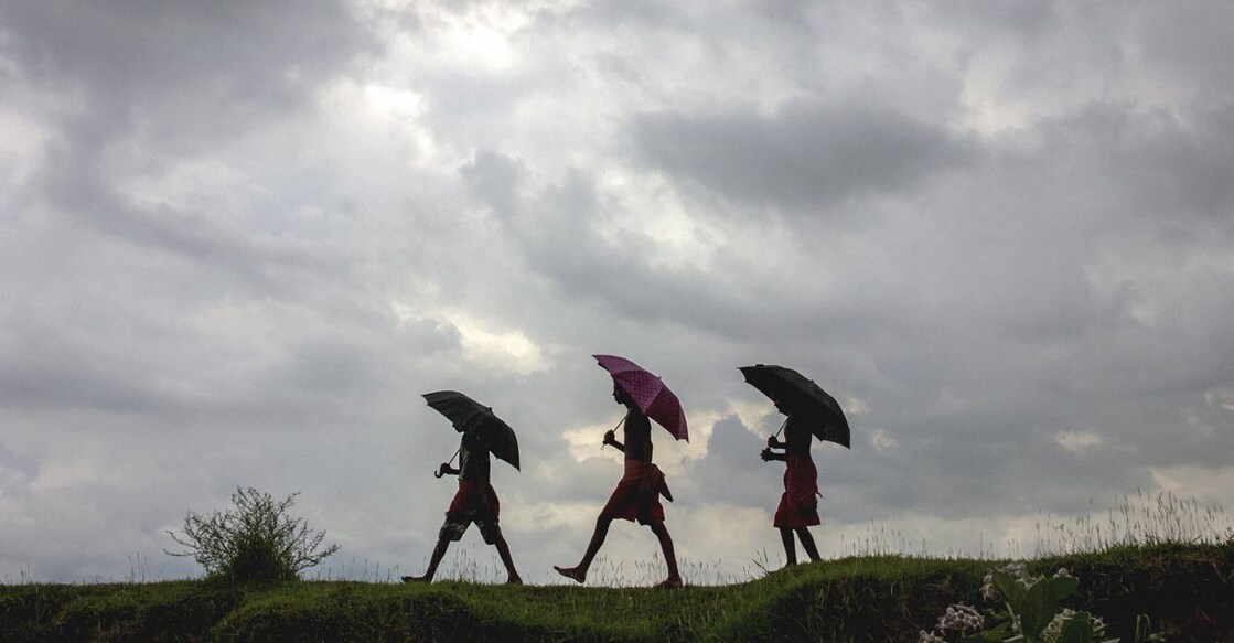 Dark clouds hover over the sky while people holding umbrellas walk amid rain, in Nadia, Saturday, July 24, 2021. PTI