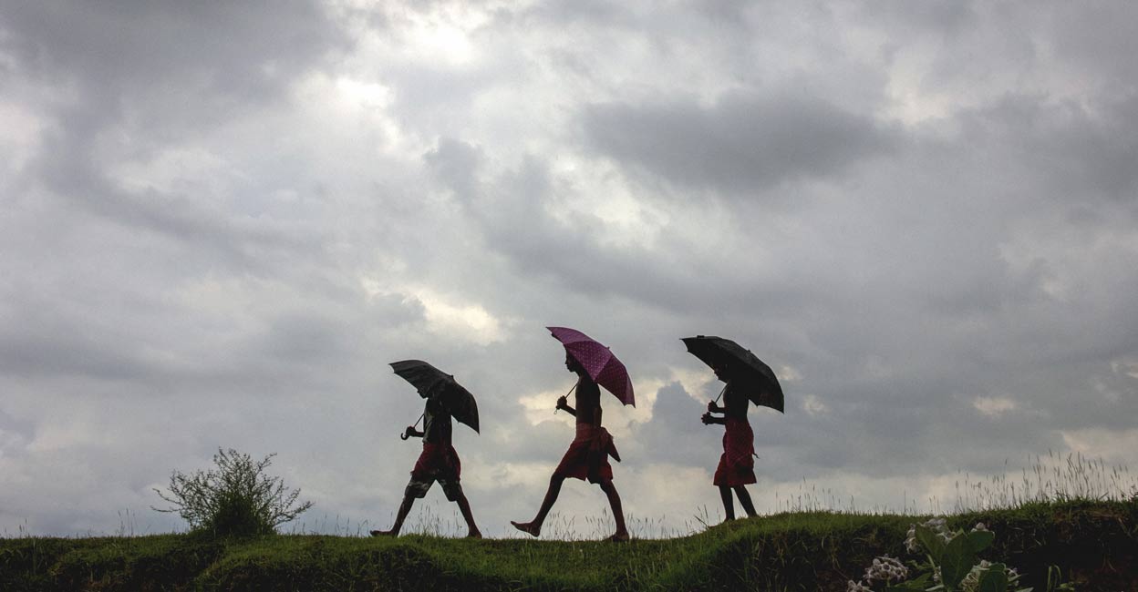 Dark clouds hover over the sky while people holding umbrellas walk amid rain, in Nadia, Saturday, July 24, 2021. PTI