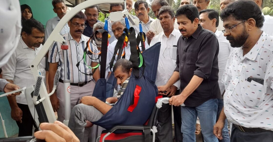 Magician and philanthropist Gopinath Muthukan hoisting Abdul Rahman, an endosulfan victim with paralysis, into an electric wheelchair in Chengala grama panchayat on Wednesday. Photo: Special Arrangement