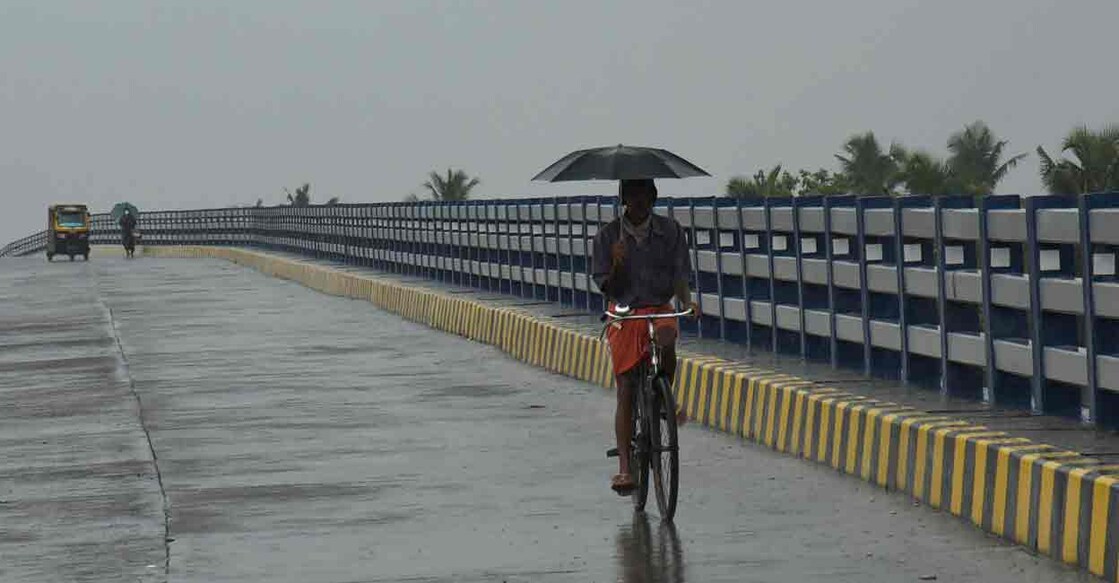 Kochi: A commuter holds an umbrella as he rides a bicycle amid rainfall ahead of the upcoming monsoon season, in Kochi, Tuesday, May 17, 2022. (PTI Photo)