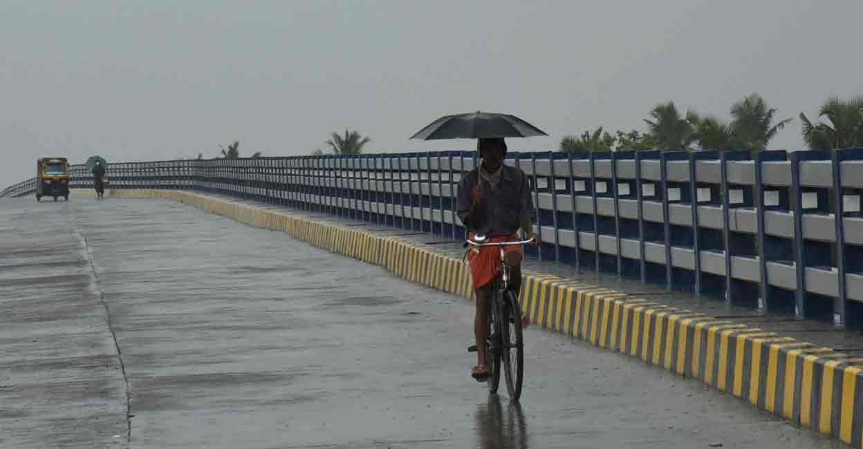 Kochi: A commuter holds an umbrella as he rides a bicycle amid rainfall ahead of the upcoming monsoon season, in Kochi, Tuesday, May 17, 2022. (PTI Photo)