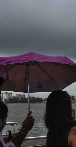 PTI05_22_2022_000155B People use an umbrella to protect themselves from the rain, as dark clouds hover in the sky in Kochi, Sunday, May 22, 2022. Photo: PTI