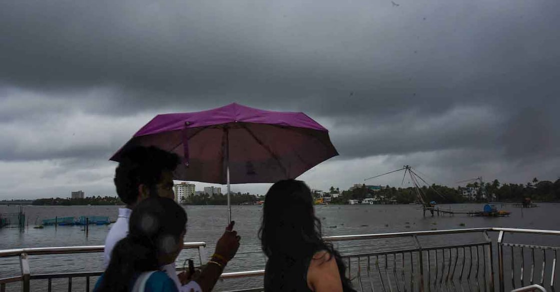 PTI05_22_2022_000155B People use an umbrella to protect themselves from the rain, as dark clouds hover in the sky in Kochi, Sunday, May 22, 2022. Photo: PTI