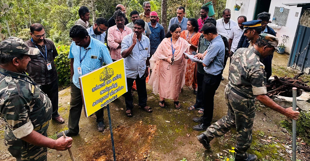 Revenue officials stand next to a state government board planted in a plot reclaimed at Chinnakanal in Idukki on Friday. Photo: Special arrangement 