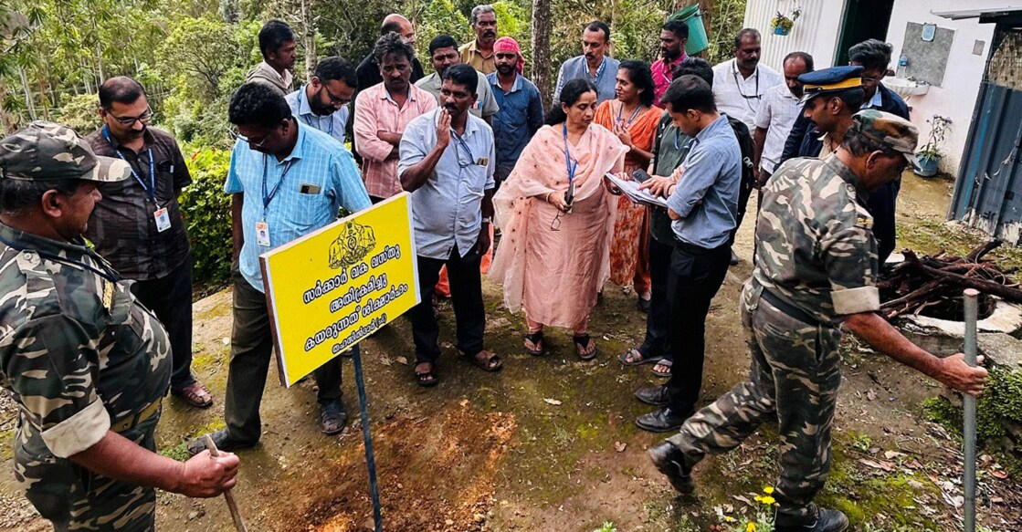 Revenue officials stand next to a state government board planted in a plot reclaimed at Chinnakanal in Idukki on Friday. Photo: Special arrangement 