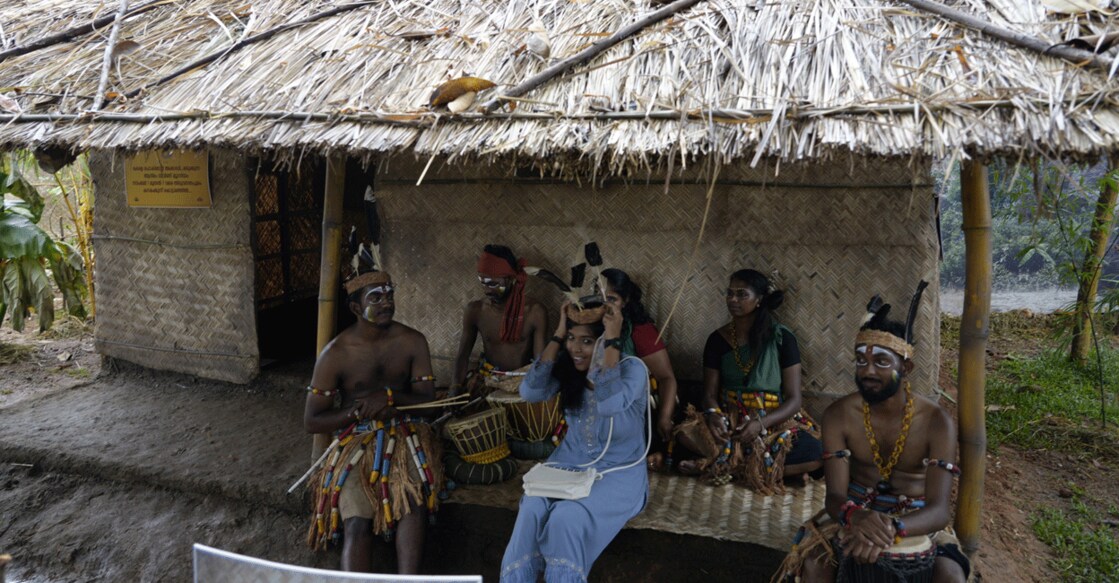 A guest poses with tribespeople in front of a makeshift traditional hut at 'Adimam' event part of Keraleeyam in Thiruvananthapuram. Photo: Facebook/@sajicheriancpim