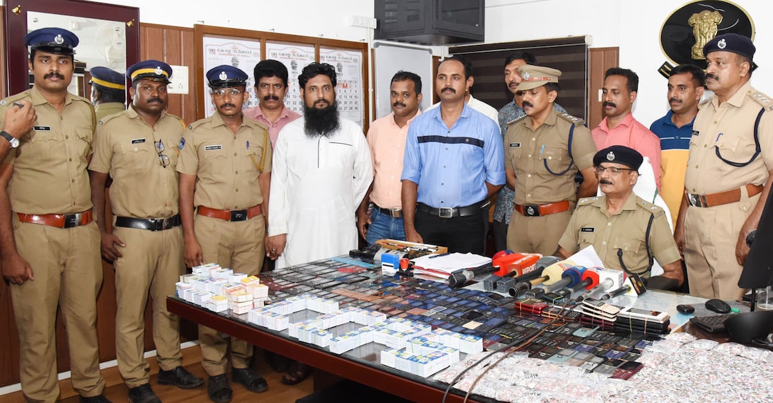 Malappuram District Police Chief S Sasidharan (sitting) and the Cyber Crime unit that arrested Abdul Roshan (white dress). The mobile phones seized from SIM cards seized from the accused can be seen on the table. Photo: Special arrangement