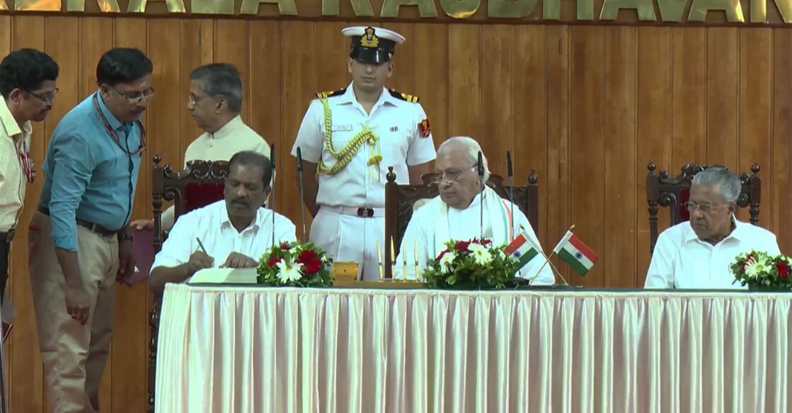 Minister O R Kelu signs after taking oath at the Raj Bhavan in the presence of Governor Arif Mohammed Khan and Chief Minister Pinarayi Vijayan. Photo: Screengrab/Facebook@keralainformation