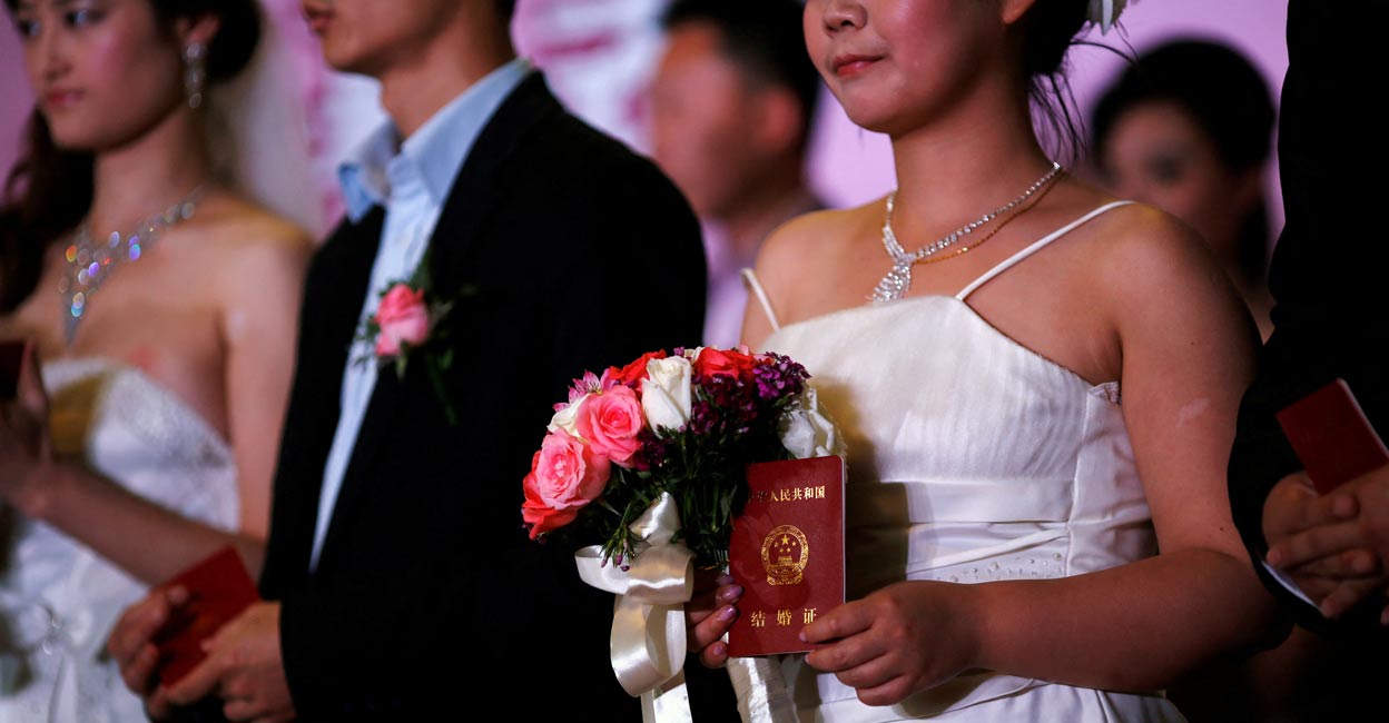 A woman holds her marriage certificate as couples participate in a staged mass wedding in a suburban area of Shanghai. Photo: REUTERS/Carlos Barria/File Photo