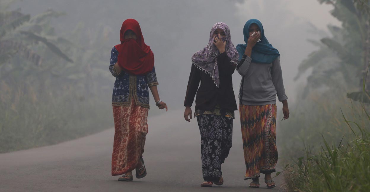 Villagers walk on a street as the haze shrouds Pulau Mentaro village in Muaro Jambi, on the Indonesian island of Sumatra. REUTERS/Beawiharta