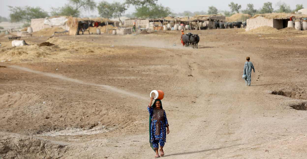 CLIMATE-CHANGE-DEADLY-TEMPERATURE A woman walks to fetch water from a nearby hand-pump with a water cooler on her head, during a heatwave, on the outskirts of Jacobabad, Pakistan. Photo: Reuters/Akhtar Soomro/File