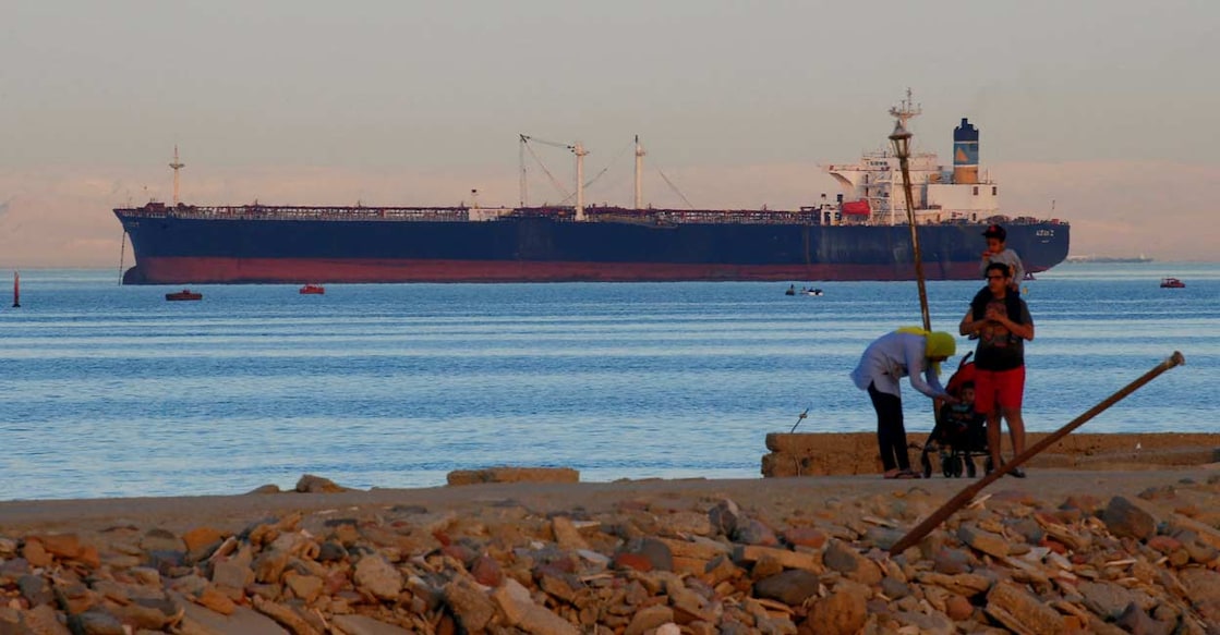 People walk on the beach as a container ship crosses the Gulf of Suez towards the Red Sea before entering the Suez Canal. Photo: Reuters/Amr Abdallah Dalsh/File