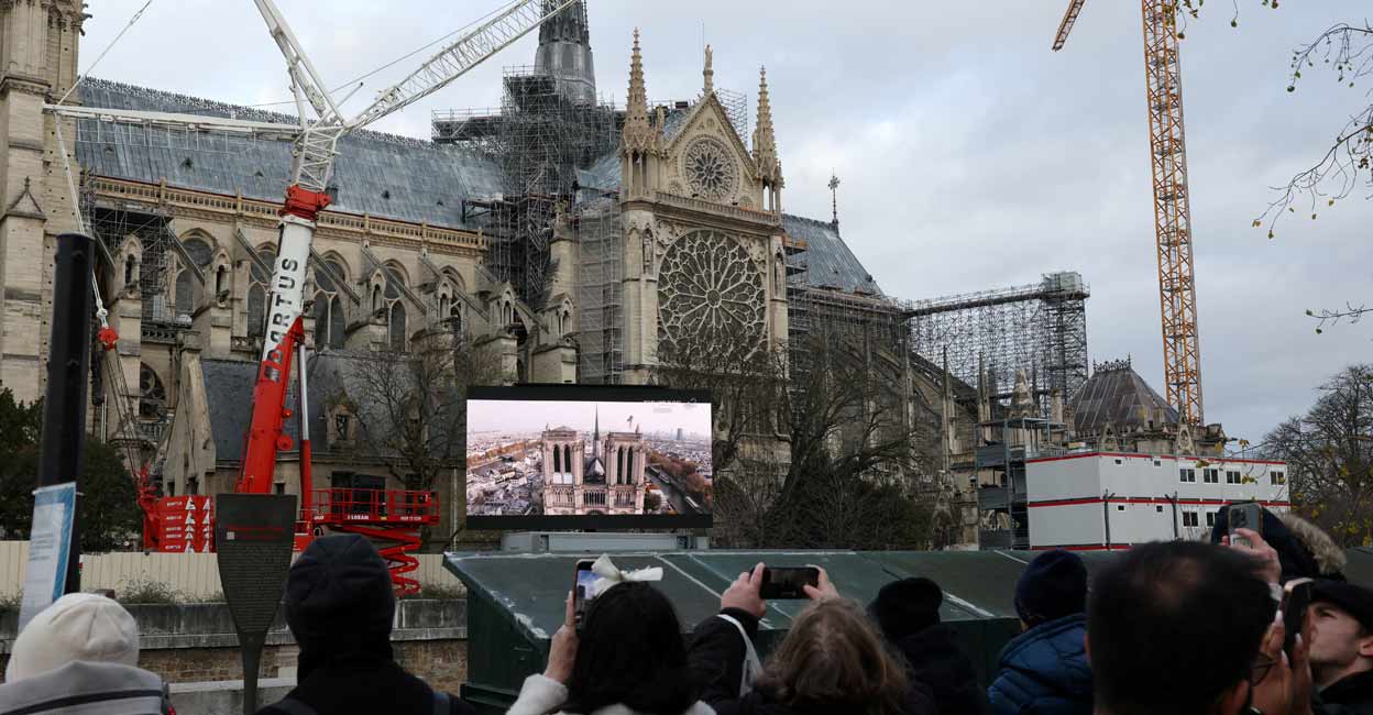FRANCE-NOTREDAME People take pictures as they stand in front of a screen in a public area to watch the reopening service ceremony of the Notre-Dame de Paris Cathedral. Photo: REUTERS/Kevin Coombs