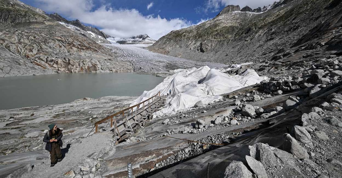 Photograph taken above Gletsch, in the Swiss Alps, in 2024 shows a woman exiting an ice cave protected by insulating fabric covering a part of the Rhone Glacier to prevent it from melting next to its glacial lake. Photo: by Fabrice COFFRINI / AFP