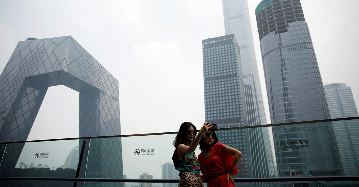 CHINA-ECONOMY-GDP Women pose for pictures at a shopping mall near the CCTV headquarters and China Zun skyscraper in Beijing's central business district (CBD). File Photo: Reuters//Tingshu Wang