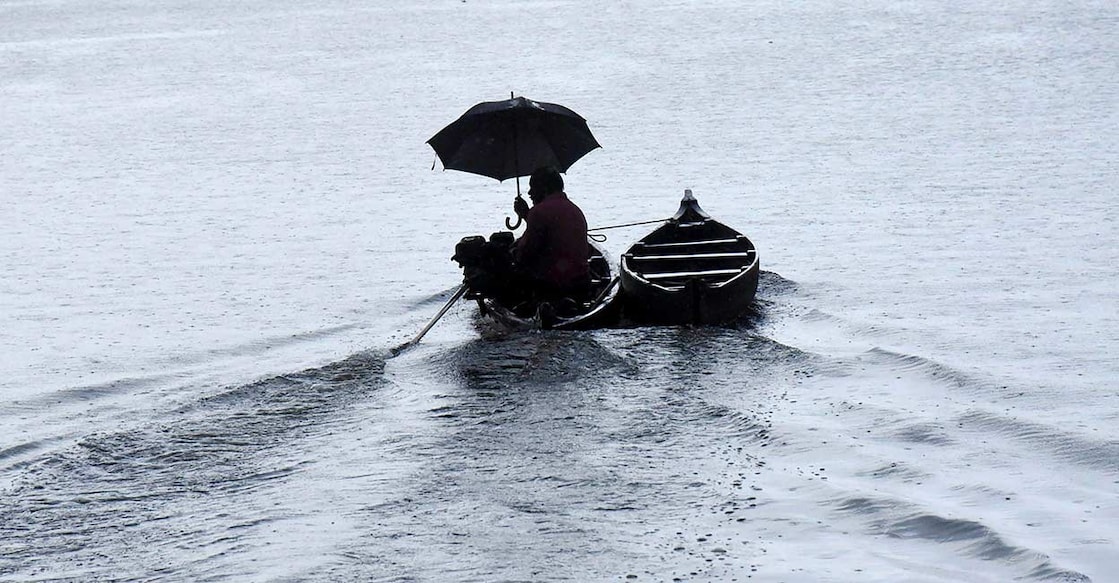 A man holds an umbrella as he rows a boat during rain after South West monsoon made landfall in Kerala. PTI