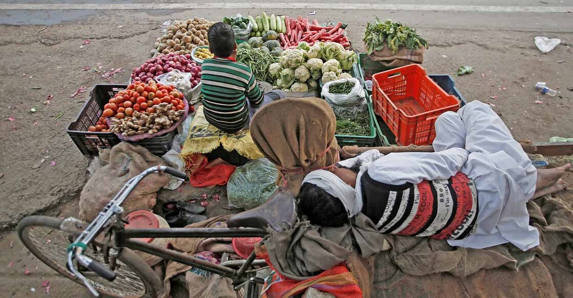 A vendor sleeps as his son waits for customers at their roadside vegetable shop in New Delhi, India, February 12, 2019. Reuters/Adnan Abidi