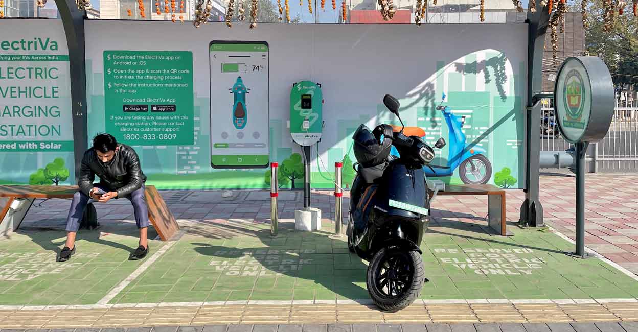 A man checks his mobile phone as he waits while recharging his Ola electric scooter at an electric vehicle charging station in New Delhi. File Photo: Reuters/Aditi Shah