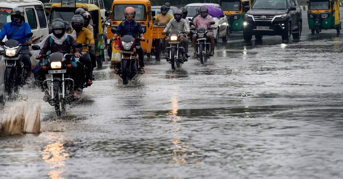 Commuters wade through a waterlogged road during rains, in New Delhi, Sunday, October 9, 2022. Photo: PTI