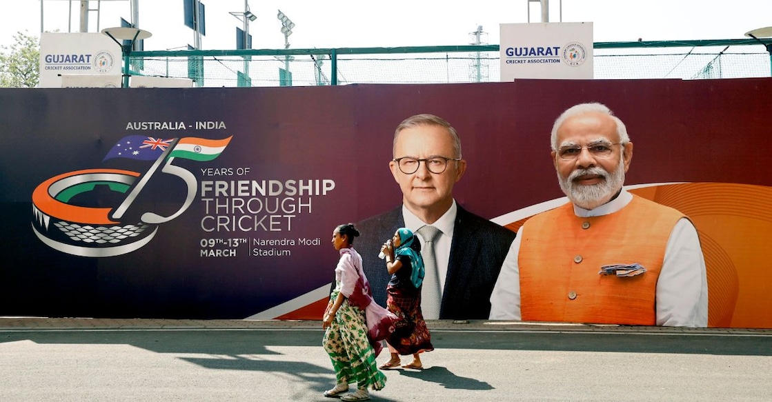 People walk past a banner of PM Modi and Australian PM Anthony Albanese ahead of their visit to watch the 4th test cricket match between India and Australia, at Narendra Modi stadium in Ahmedabad, Wednesday, March 8, 2023. Photo: PTI