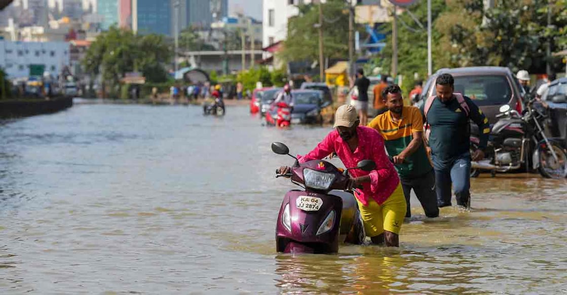 Commuters push their two-wheelers through a waterlogged road after heavy rain, near Kendriya Vihar apartment, in Bengaluru, Karnataka, Tuesday, Oct. 22, 2024. Photo: PTI