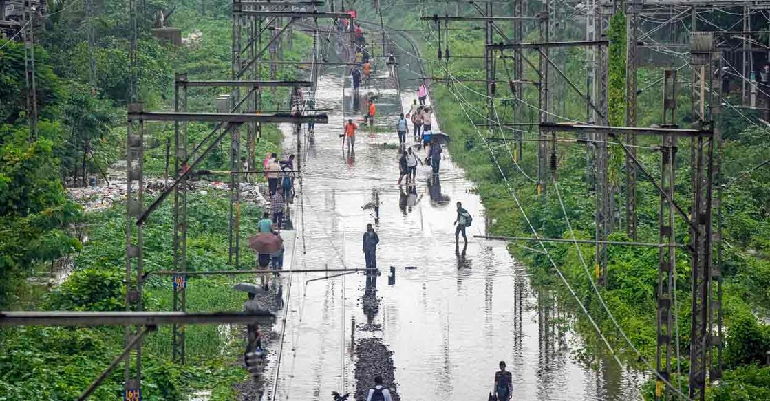 People walk through a waterlogged railway track following rains, in Mumbai, Monday, July 8, 2024. Photo: Shashank Parade/PTI