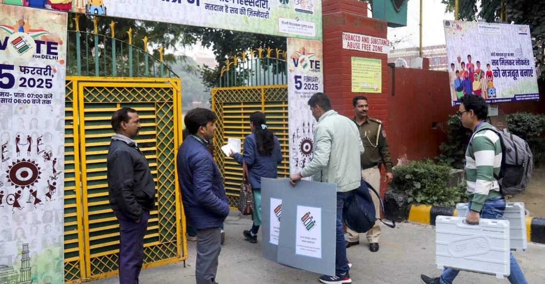 Polling officials carrying EVMs and other election materials arrive at a polling centre at Gole Market ahead of Delhi Assembly poll, in New Delhi. Photo: PTI