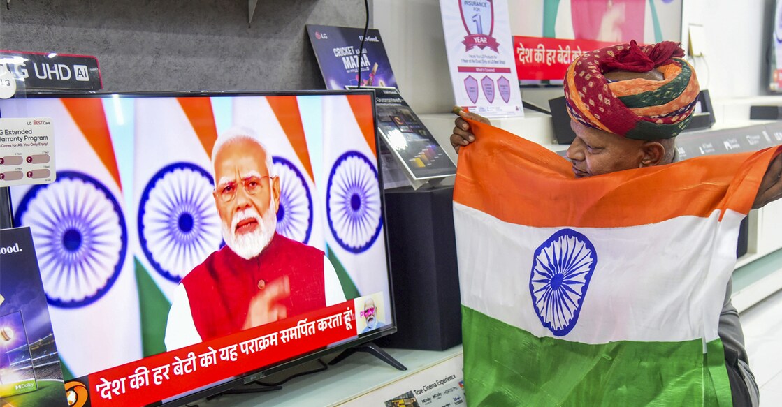 A man holds the national flag as he watches the live telecast of Prime Minister Narendra Modi's address to the Nation, in Bikaner, Monday, May 12, 2025. Photo: PTI
