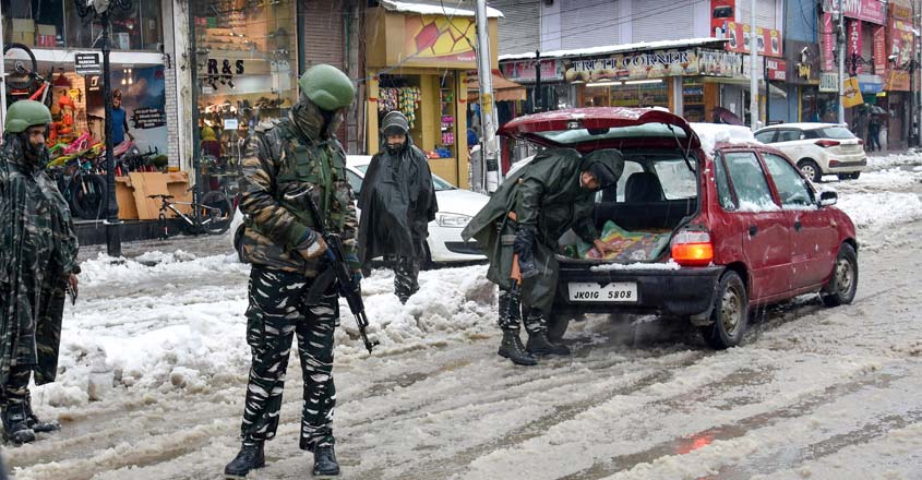 PTI1_13_2020_000102B A security personnel checks a vehicle as others stand guard during snowfall, in Srinagar, Monday, Jan. 13, 2020. Snowfall in Kashmir threw life out of gear for the second day on Monday and forced cancellation of all flights to and fro Srinagar airport. (PTI Photo)