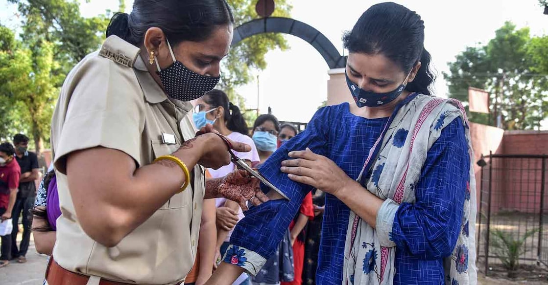 A security woman uses scissors to make the dress of a female candidate half-sleeve as she arrives to appear in Rajasthan Administrative Services (RAS) 2021 prelims exam, at a centre in Bikaner, Wednesday, Oct 27, 2021. RPSC has allowed female candidates to wear salwar suit, saree, half sleeve kurta or blouse, slippers. Photo: PTI