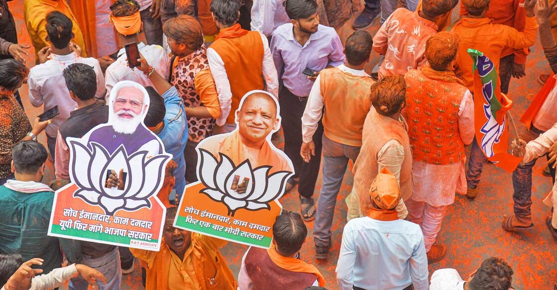 BJP supporters holding cutouts of Prime Minister Narendra Modi and UP Chief Minister Yogi Adityanath celebrate with colours as the party heads to a landslide victory in UP Assembly elections in Lucknow on March 10, 2022. Photo: PTI