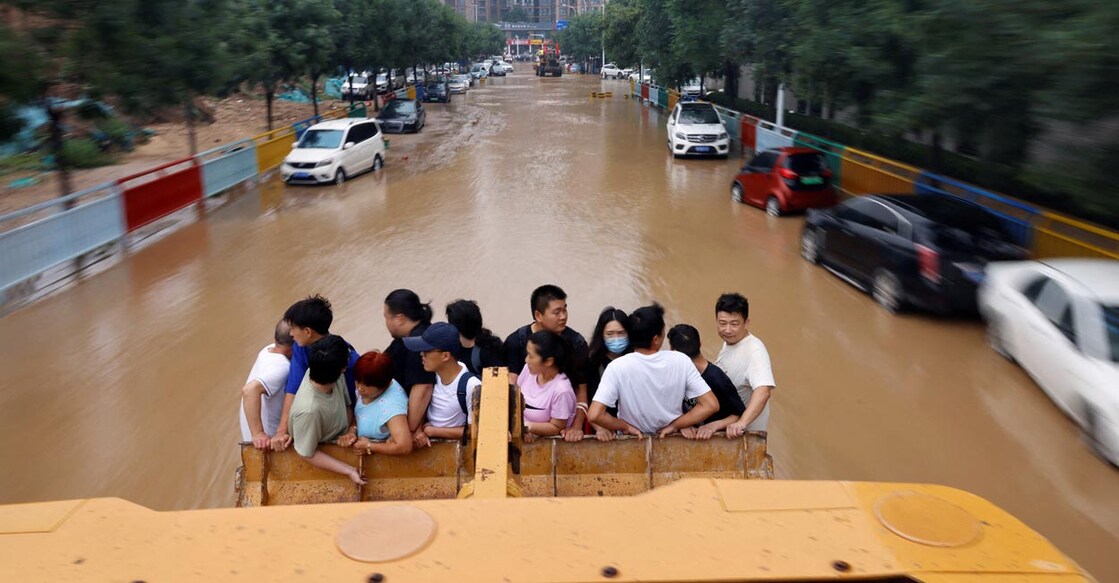 Henan flood People ride on a front loader as they make their way through a flooded road following heavy rainfall in Zhengzhou, Henan province, China, July 23, 2021. Photo: REUTERS/Aly Song